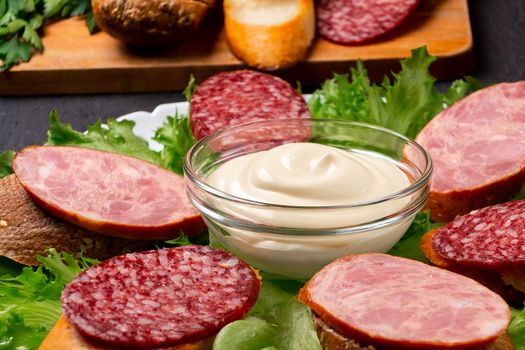 Several sandwiches with sausage and salami and sauce on a plate, close up.