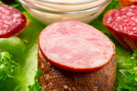 Several sandwiches with sausage and salami and sauce on a plate, close up.