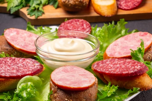 Several sandwiches with sausage and salami and sauce on a plate, close up.