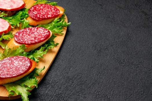 Several sandwiches with sausage and salami and sauce on a black board, flat lay background with copyspace.