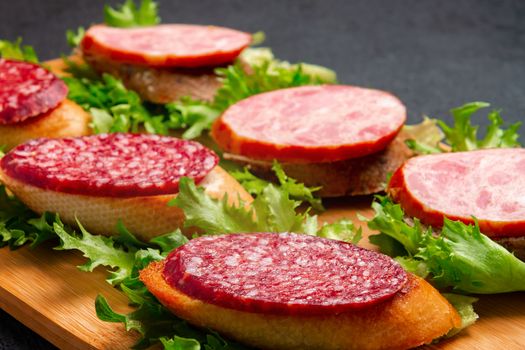 Several sandwiches with sausage and salami and sauce on a black board, flat lay background with copyspace.