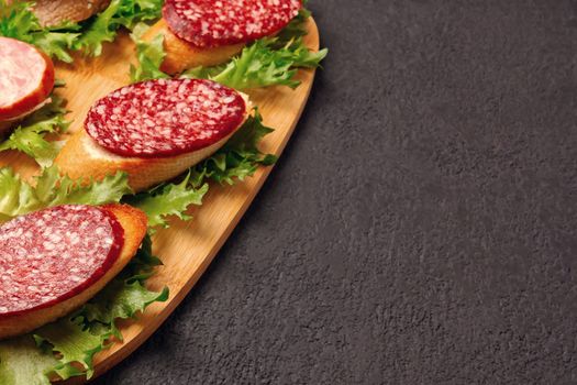 Several sandwiches with sausage and salami and sauce on a black board, flat lay background with copyspace.