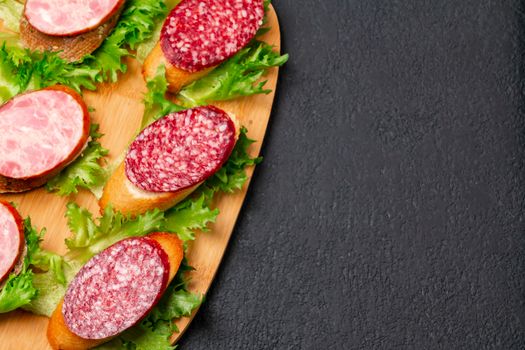 Several sandwiches with sausage and salami and sauce on a black board, flat lay background with copyspace.