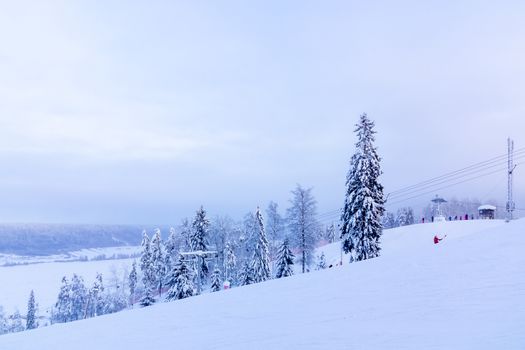 Snow-covered ski slope in the mountains with a lift and skiers skating away.