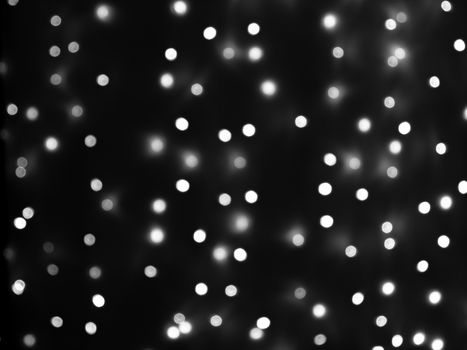 Defocused lights of Christmas garland in black and white evenly distributed over the area of the frame, background, texture.