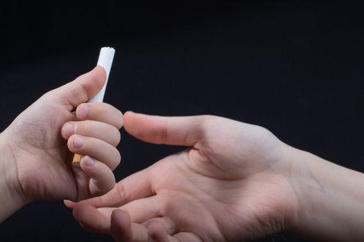 Hand is giving out cigarette on a black background