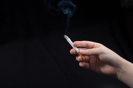 Hand is holding smoking cigarette with smoke around