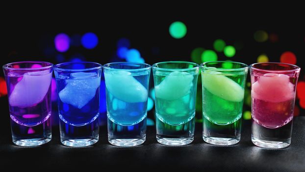 Variation of hard alcoholic shots with ice served on bar counter. Blur neon background