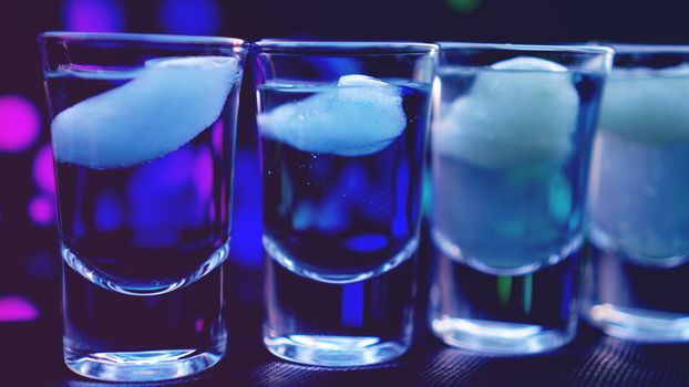 Glasses of vodka with ice. In bar - neon background
