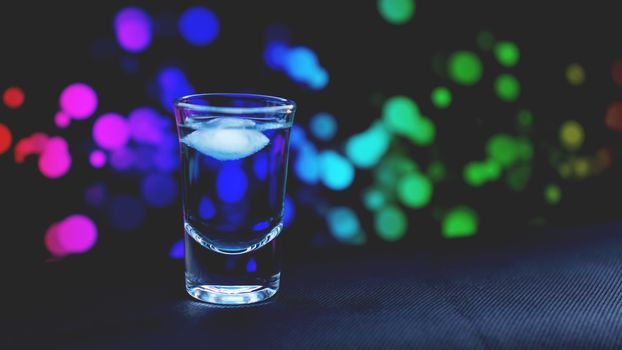 Drink shot with ice in bar on neon color abstract background