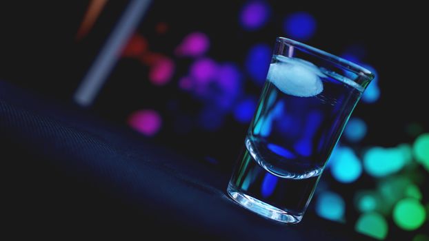 Drink shot with ice in bar on neon color abstract background