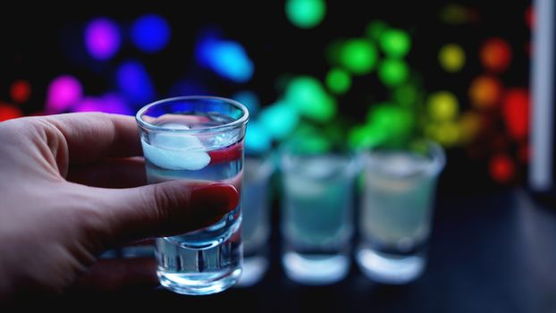 Female hand with a shot of alcohol, neon blurred background in bar