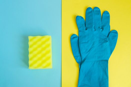 Professional concept of cleaning the house, accessories for a spring cleaning, blue rubber gloves and cleaning sponge on a double yellow and blue background, flat lay.