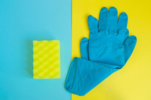 Professional concept of cleaning the house, accessories for a spring cleaning, blue rubber gloves and cleaning sponge on a double yellow and blue background, flat lay.