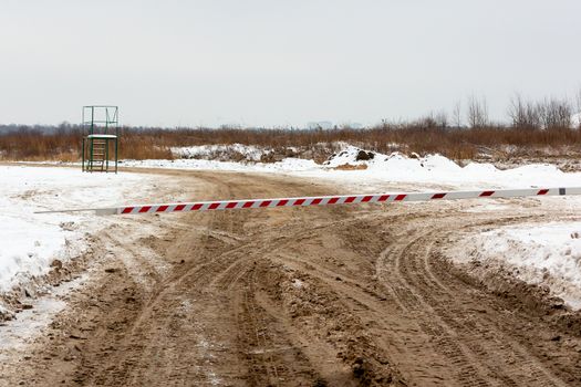 Dirty winter road, blocked by a barrier closing the entrance.