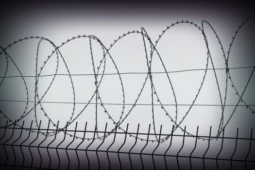 Metal fence with barbed wire on top against the sky.