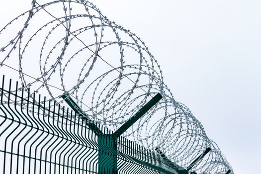 Metal fence with barbed wire on top against the sky.