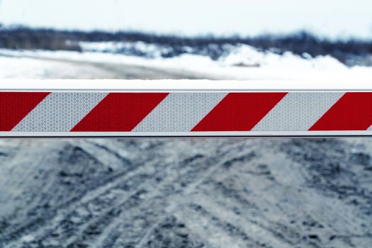 Dirty winter road, blocked by a barrier closing the entrance.