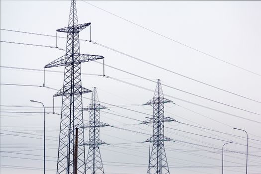 Power line towers with wires against a cloudy sky.