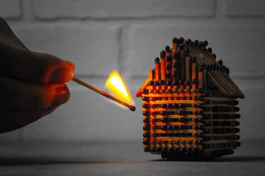 hand with a burning match sets fire to the house model of matches, risk, property Insurance protection or ignition of combustible materials concept.