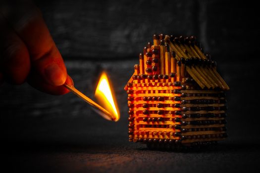 hand with a burning match sets fire to the house model of matches, risk, property Insurance protection or ignition of combustible materials concept.