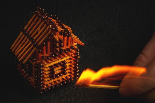 hand with a burning match sets fire to the house model of matches, risk, property Insurance protection or ignition of combustible materials concept.