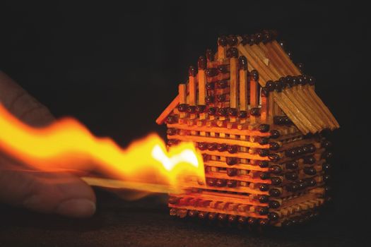 hand with a burning match sets fire to the house model of matches, risk, property Insurance protection or ignition of combustible materials concept.