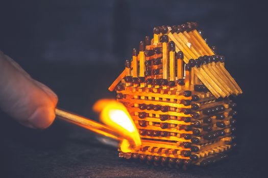 hand with a burning match sets fire to the house model of matches, risk, property Insurance protection or ignition of combustible materials concept.