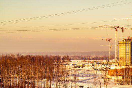 Construction on the outskirts of the city - construction equipment, cranes, started houses, surrounded by fields and cut down forests.