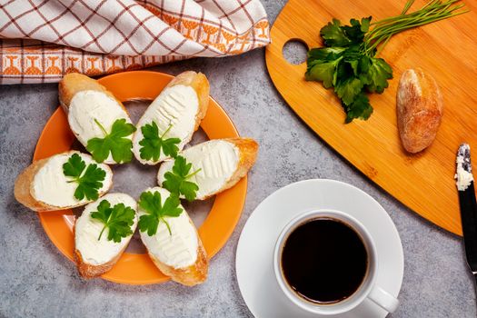 Freshly made sandwiches with cream cheese and parsley on a plate, chopping wooden board and a cup of coffee - morning and breakfast concept, top view.