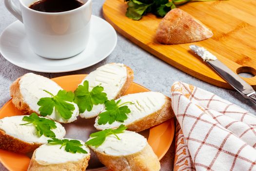 Freshly made sandwiches with cream cheese and parsley on a plate, chopping wooden board and a cup of coffee - morning and breakfast concept.