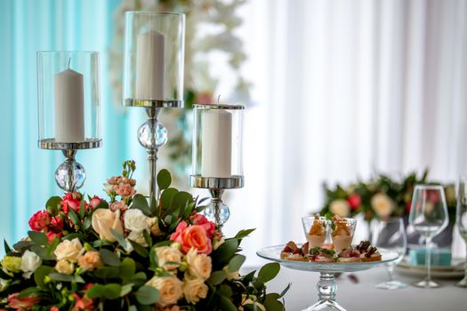 Wedding table decoration. Candlestick with candles, bouquet of flowers and salads in plate on the wedding table.