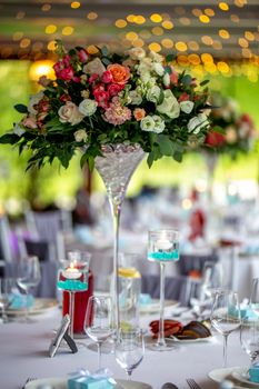 Wedding table decoration. Beautiful bouquet of flowers in vase on the table, next to plates,  glasses and gift boxes. Bouquet of flowers, glasses, gift boxes and jugs setting on the festive table in restaurant.