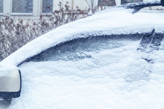 Snowfall in the city, part of the car covered by snow.