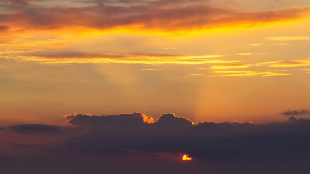 sky during a colorful, bright orange sunset, sun's rays make their way through the clouds.