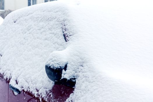 Snowfall in the city, part of the car covered by snow.