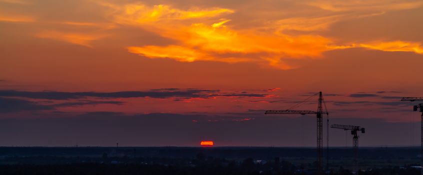 Several construction cranes on the background of colorful sunset sky.