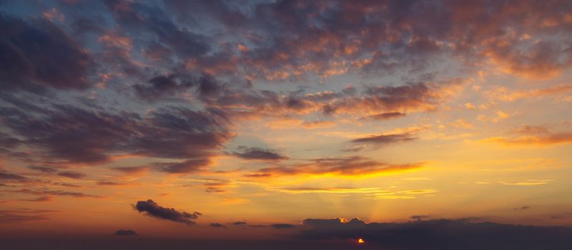 sky during a colorful, bright orange sunset, sun's rays make their way through the clouds.