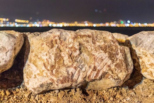 a shoot with far city lights behind sea and focus on white rocks. photo has taken at izmir/turkey.