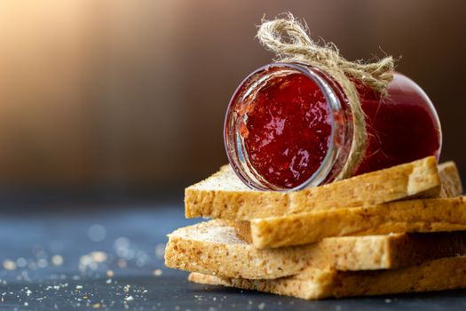 Strawberry jam bottle and whole wheat bread are stacked on a black background. Concept of breakfast and healthy food.