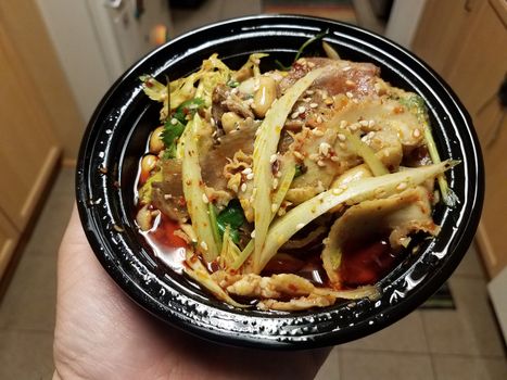 hand holding bowl of Chinese beef and intestine slices in spicy oil with peanuts in kitchen