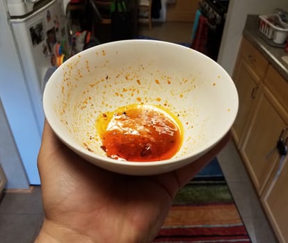 hand holding white bowl of red greasy oil in kitchen