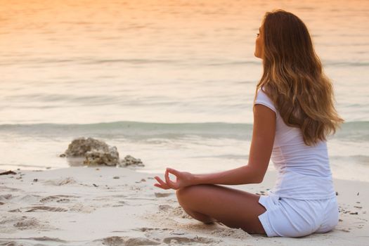 Young healthy woman practicing yoga on the beach at sunset