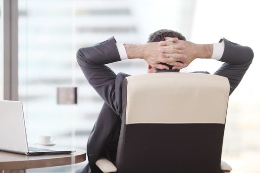 Businessman relaxes sitting in the office and looking in window