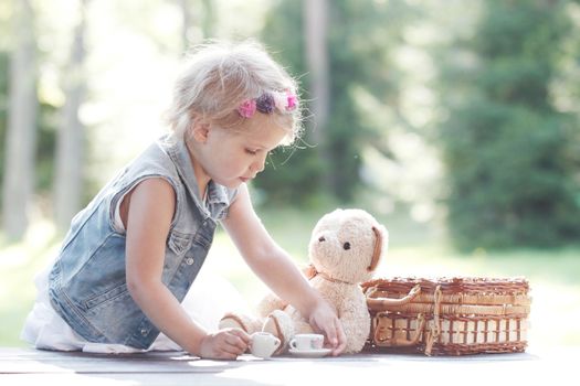 Pretty girl playing with teddy bear outdoors