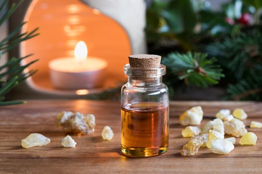 A bottle of frankincense essential oil with frankincense resin crystals, spruce and pine branches, and an aroma lamp in the background
