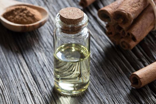 A bottle of cinnamon essential oil on old wood, with cinnamon sticks and ground cinnamon in the background