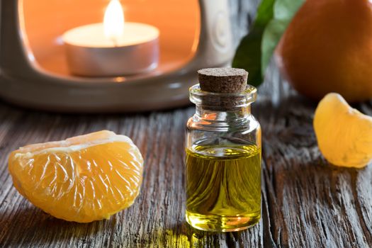 A bottle of tangerine essential oil on a wooden table, with fresh tangerines and an aroma lamp in the background