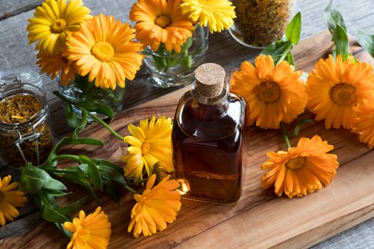 A bottle of calendula (marigold) tincture on a wooden table, with fresh and dry calendula flowers in the background