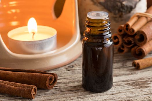 A bottle of cinnamon essential oil with cinnamon sticks and an aroma lamp in the background